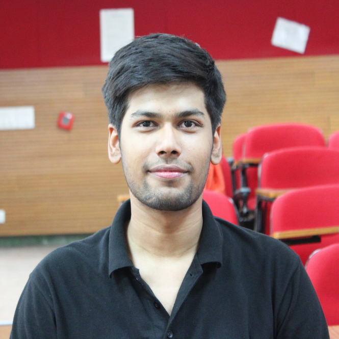 Divyanshu wearing a tshirt, in a lecture hall, smiling.